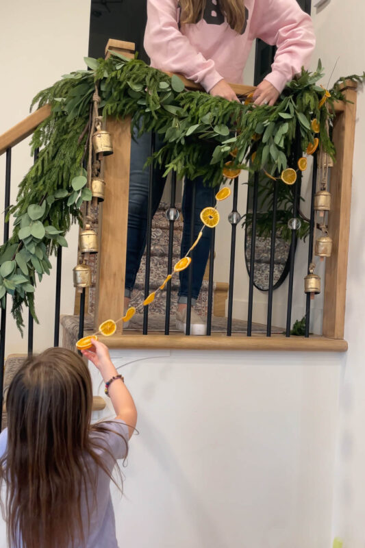 Wrapping an orange slice garland on a stair banister.